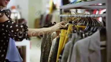 漂亮的年轻女子正拿着一件连衣裙，在商场的服装店里寻找另一件连衣裙